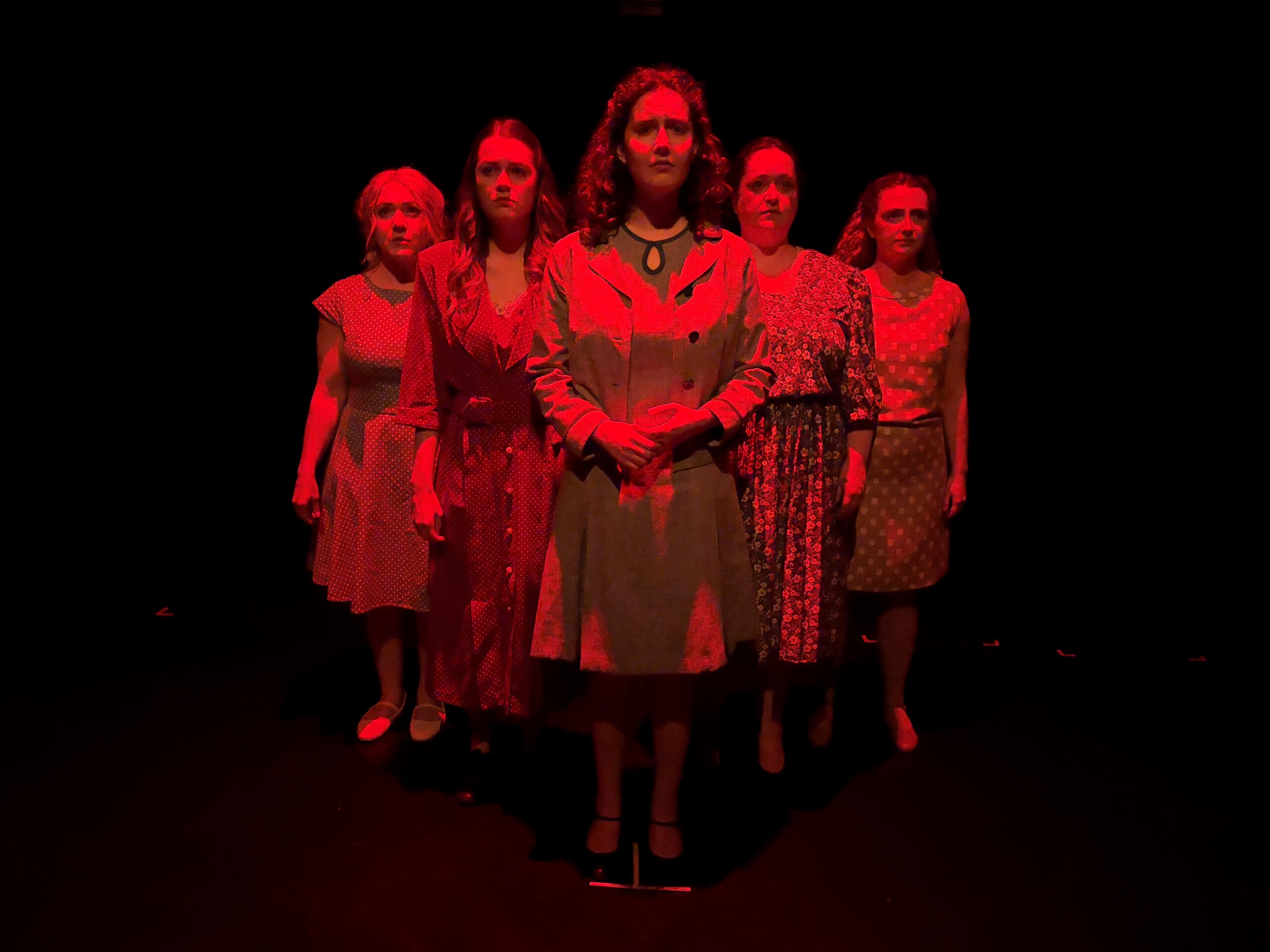 Five actresses standing together under red light.