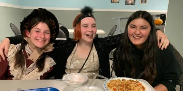 Three people wearing costumes are smiling at the camera over lunch.
